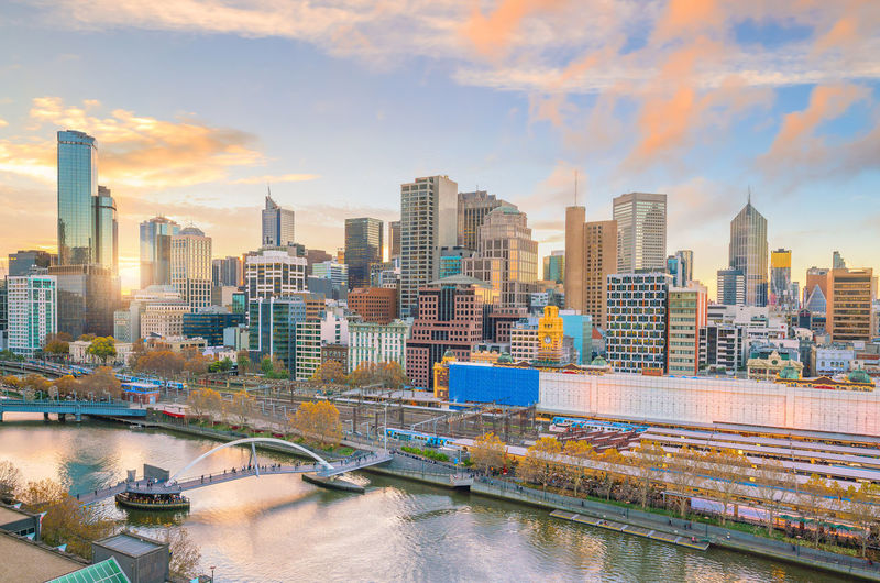 Bridge over river amidst buildings against sky during sunset