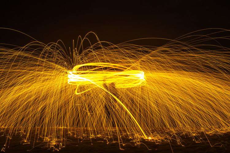 Long exposure silhouette of unrecognizable person spinning burning stick emitting sparkles while dancing with fire at night