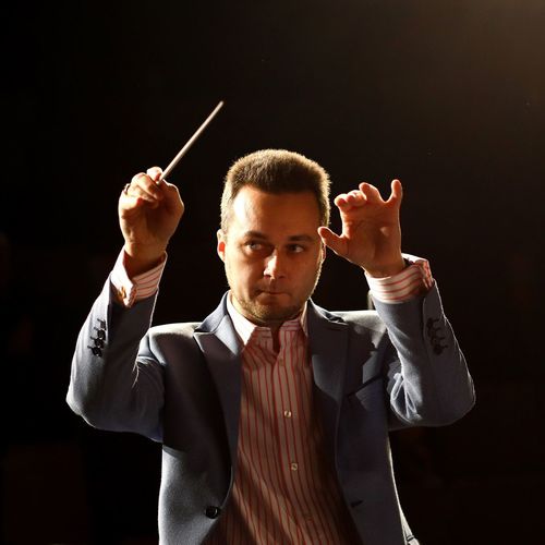 Male musical conductor conducting against black background