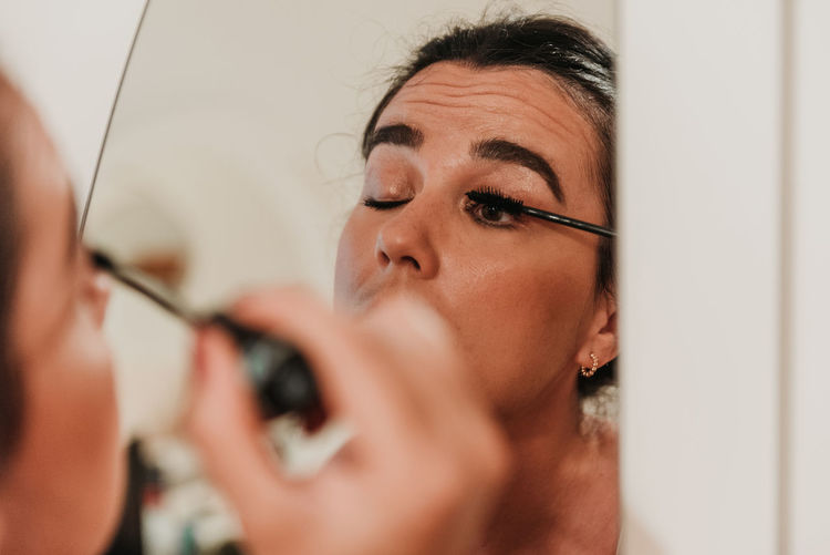 Mirror photo of beautiful young woman putting on makeup