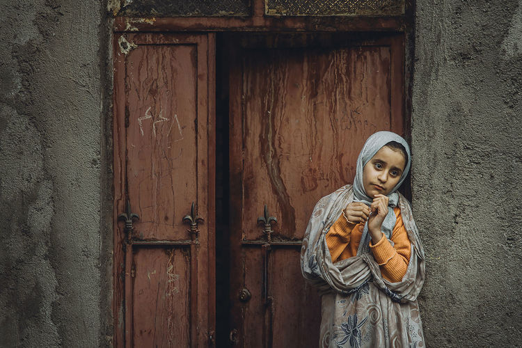 Thoughtful young woman wearing hijab standing against door