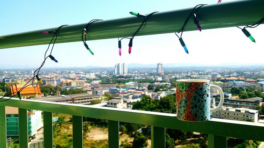 Coffee mug on railing with christmas lights against city seen from balcony