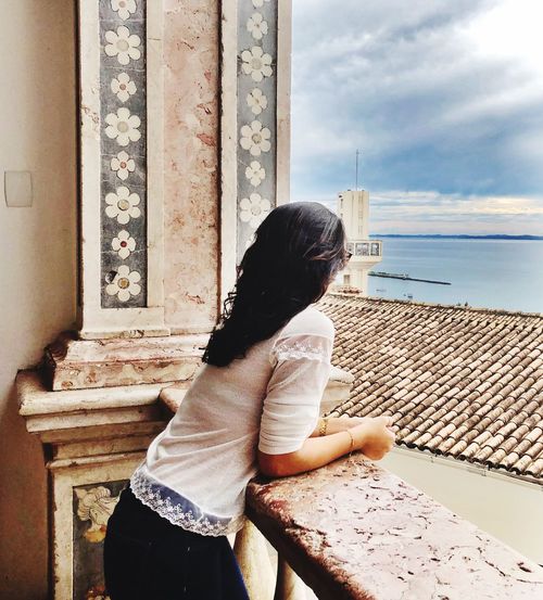 Side view of woman looking at sea while leaning on railing against sky