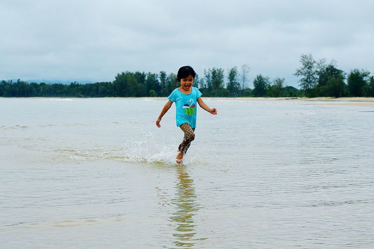 Full length portrait of happy boy playing on beach against sky