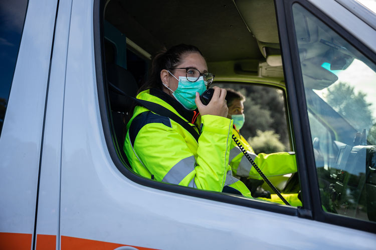 Woman wearing mask talking on cb radio while sitting at ambulance