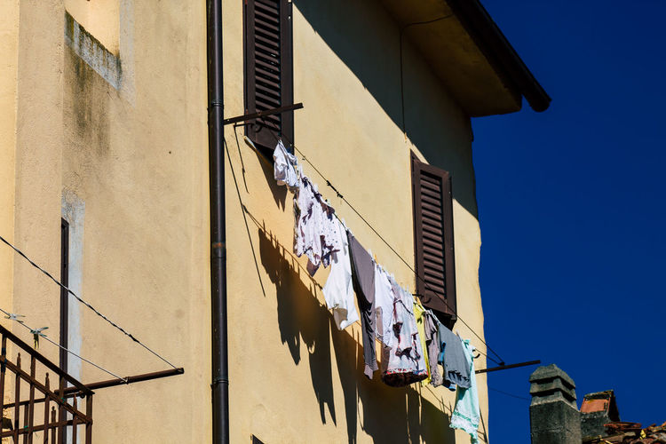 Low angle view of laundry drying on clothesline of residential building against clear blue sky