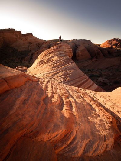 Distant view of young man standing on rock formation against sky