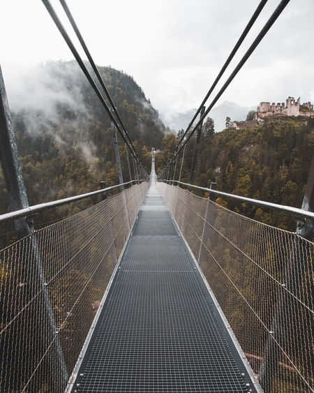Diminishing perspective of footbridge against cloudy sky