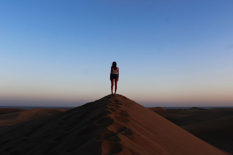 Full length of woman standing on sand dune against sky during sunset