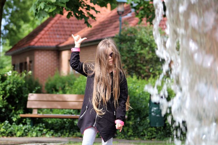 Girl with long hair gesturing shaka sign while standing at yard
