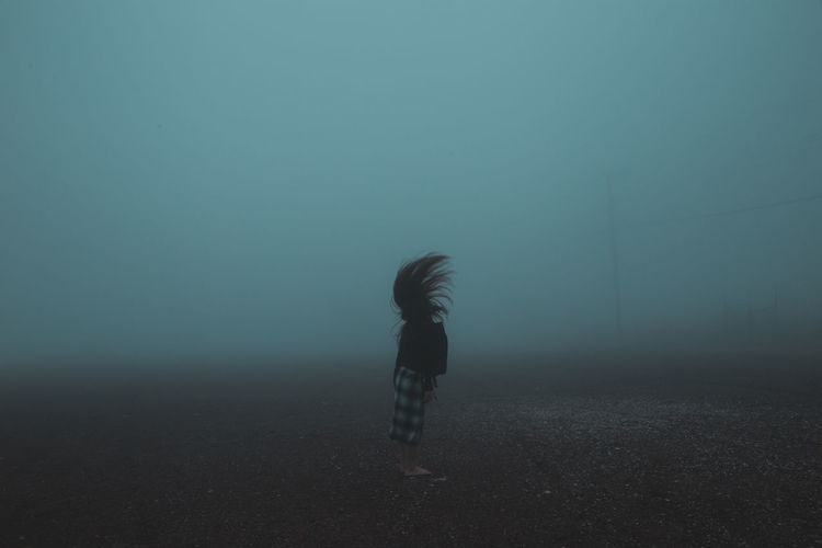 Side view of woman tossing hair while standing on field during foggy weather