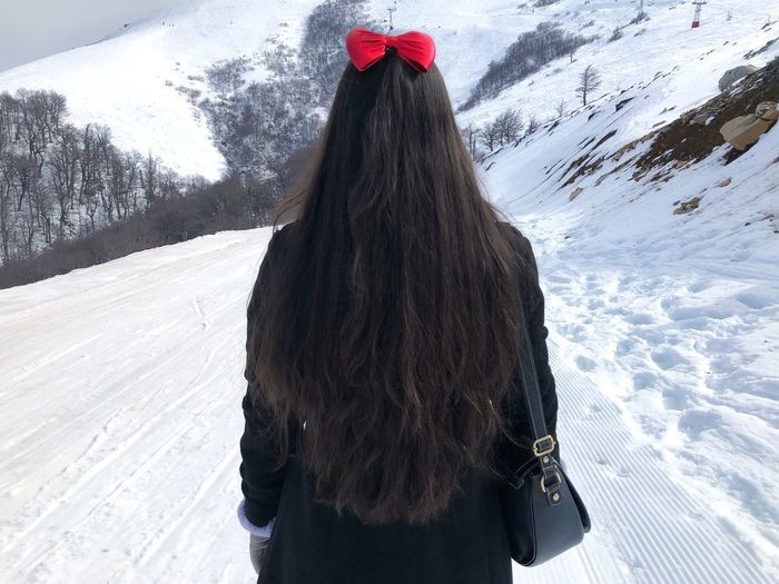 Rear view of young woman with long hair standing on snow covered landscape