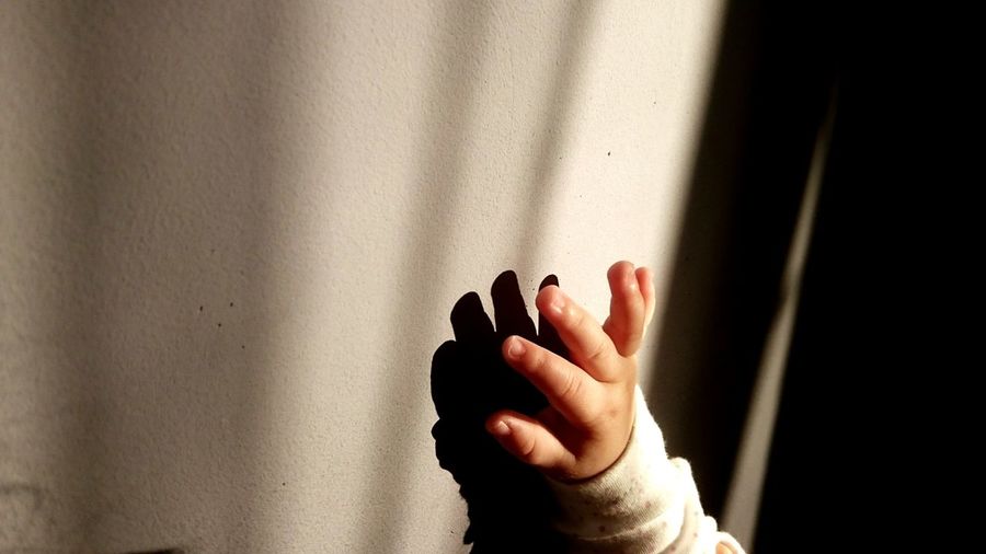 Cropped hand of baby girl by wall with shadow