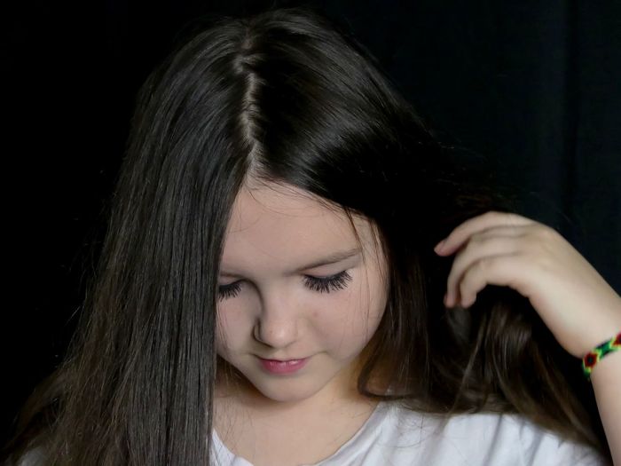 Close-up of teenage girl with long black hair against black background