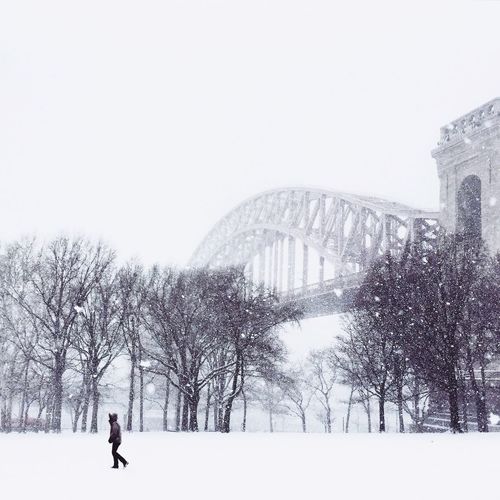 Man walking on snow covered astoria park by hells gate bridge against clear sky
