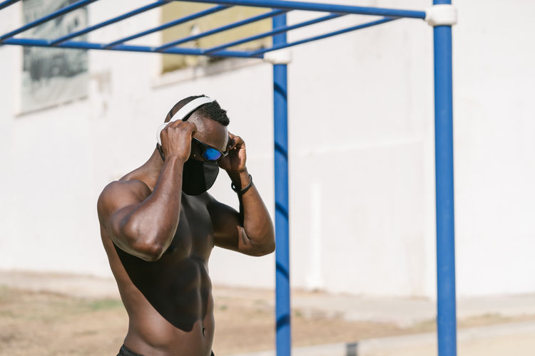 Full length of shirtless athletic african american male doing exercise on fitness equipment while training alone on sports ground