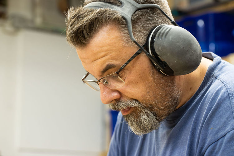 Manual worker wearing eyeglasses and ear protectors working in workshop
