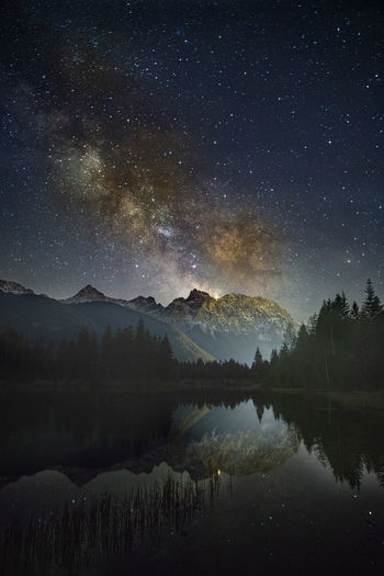 Scenic view of lake and mountains against star field in sky
