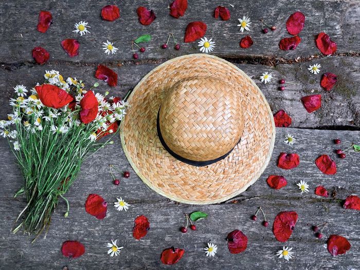 Summer flat lay consisting of straw hat, flower bouquet and poppy petals on a rustic wooden table