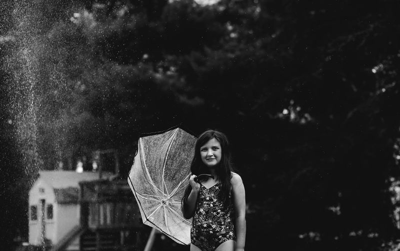 Girl holding umbrella while standing against trees