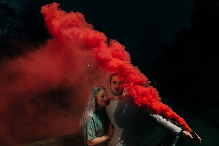 Man embracing woman while holding distress flare at night