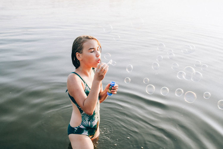 Teenage girl blowing bubbles while standing in lake