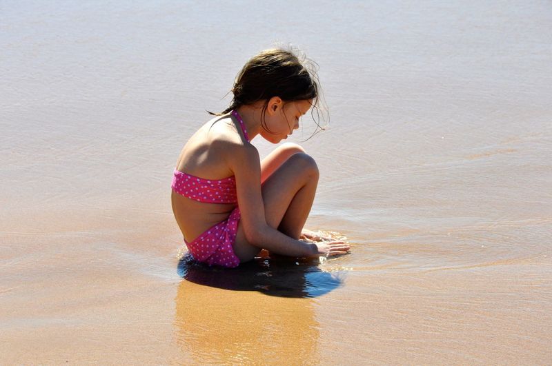 Side view of girl wearing swimwear sitting at shore