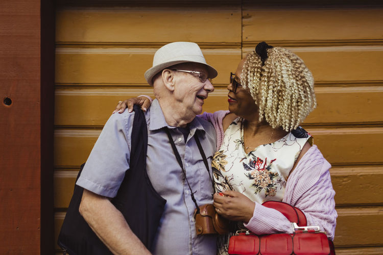 Smiling senior couple with arms around against wall