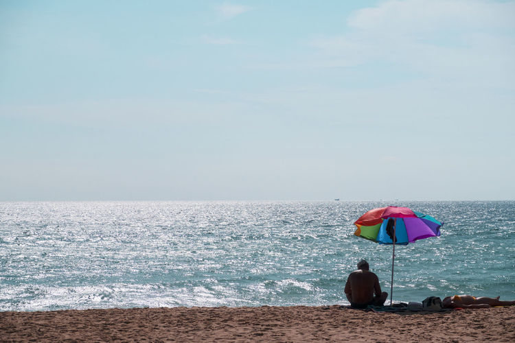 Man and woman resting at beach against sky