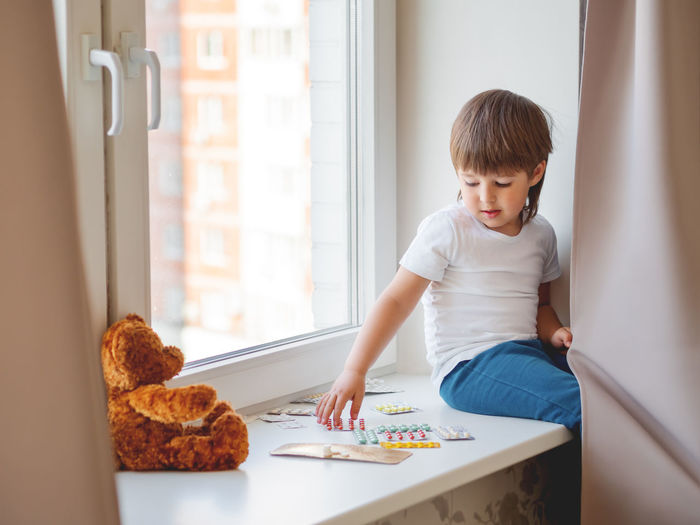 Toddler sits on windowsill and plays with scattering pills without parent's control. 
