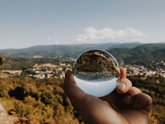 Cropped hand of person holding crystal ball on mountain against sky