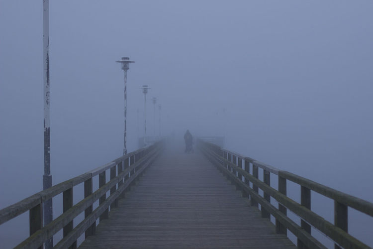 Footbridge walking on pier against sky during foggy weather