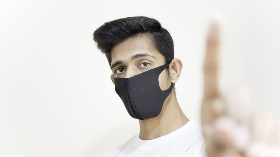 Portrait of young man covering face against white background