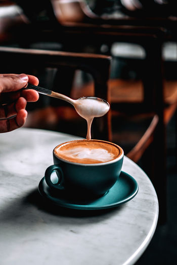 Hand holding coffee foam using a spoon from a cup