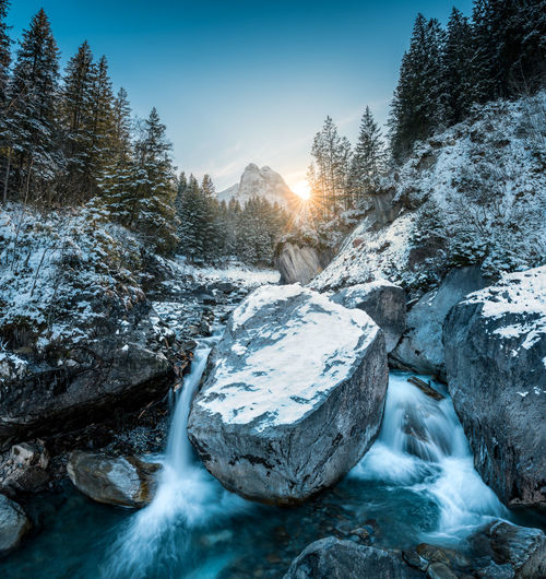 Frozen river amidst rocks against sky during winter