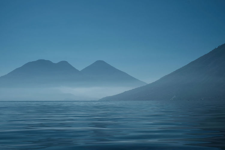 Scenic view of sea and mountains against clear blue sky