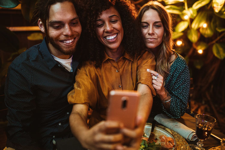 Smiling woman taking selfie with friends while sitting outdoors