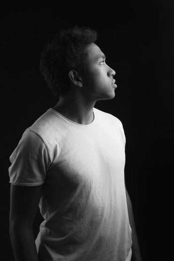 Side view of young man looking away against black background