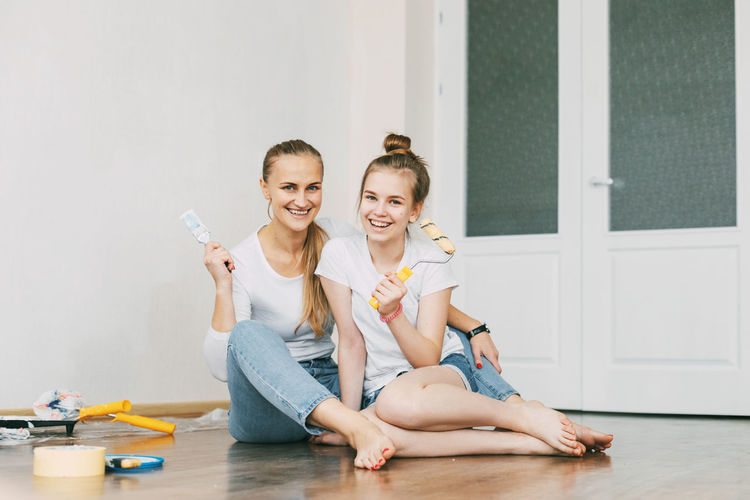 Beautiful and happy mom and daughter paint the walls in the apartment white