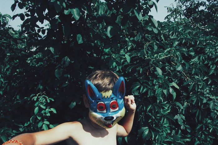 Shirtless boy wearing mask against plants