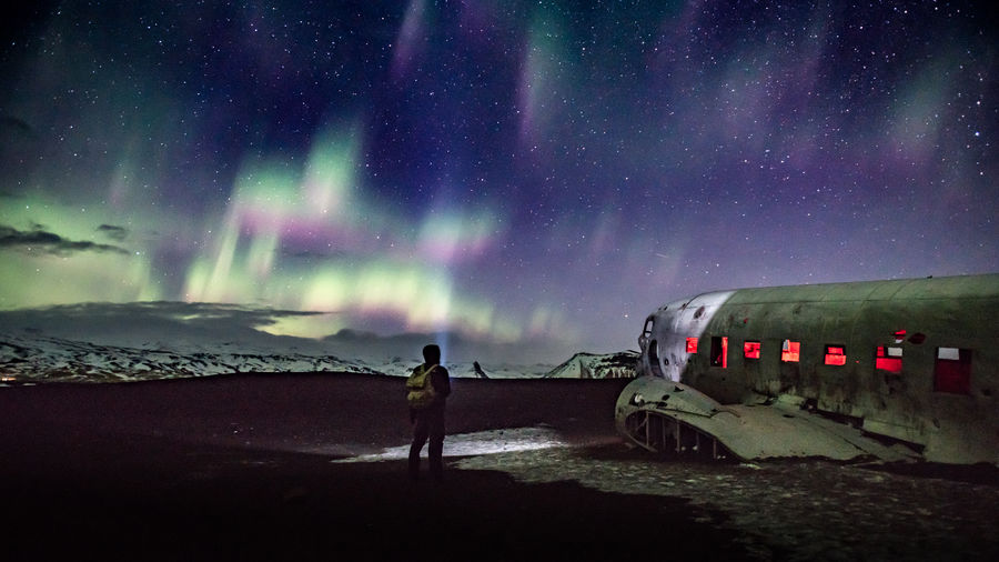 Rear view of man looking at abandoned ship in sea against sky during night