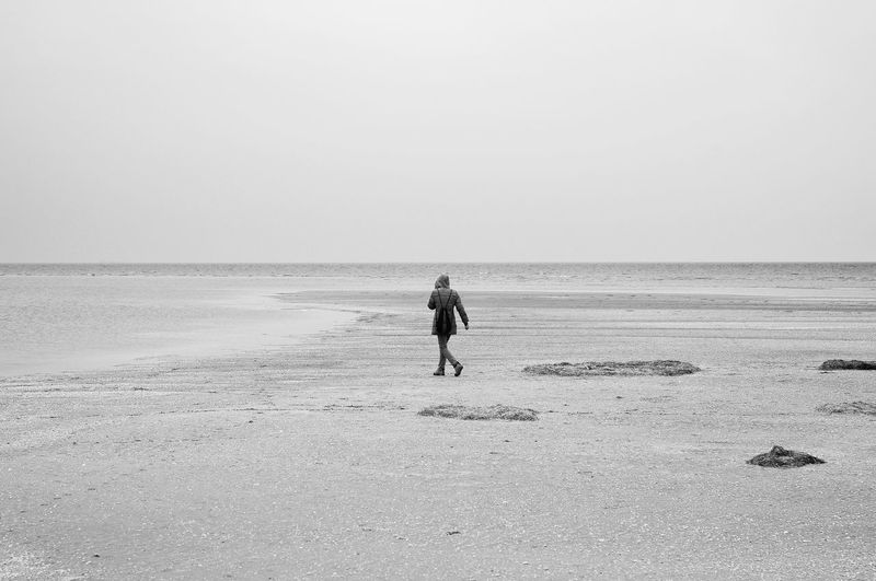 Rear view of woman walking at beach against clear sky