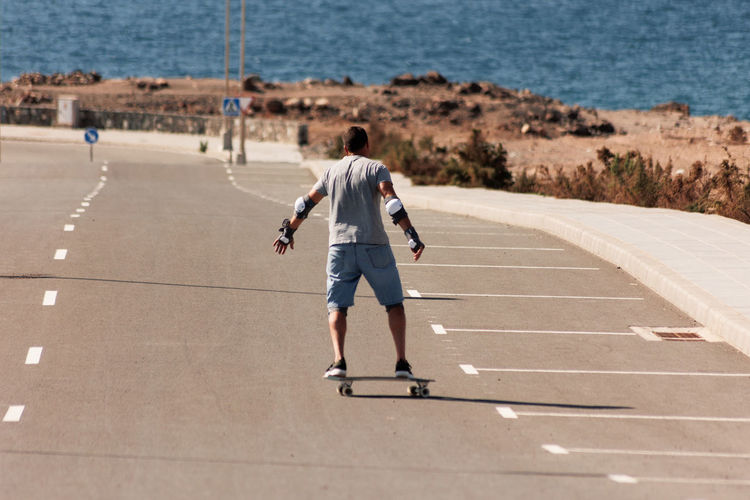 A man playing figure skating on a rural road in the sun on a bright day,play surf skate near coast