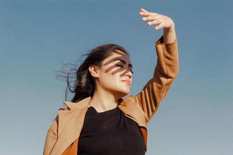 Young woman with arms raised against clear sky
