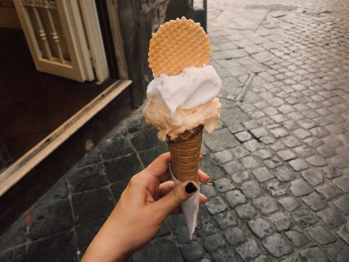 Close-up of hand holding ice cream cone on footpath