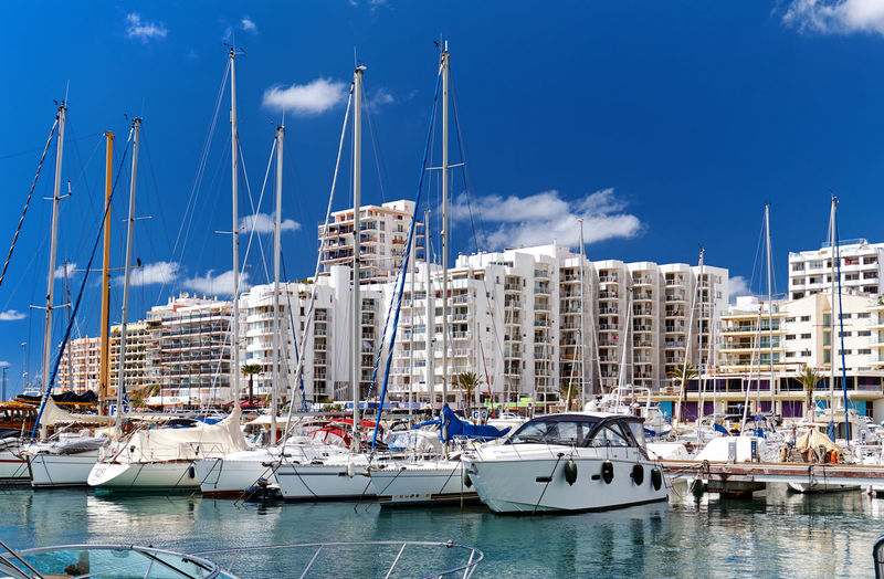 Sailboats moored in harbor against buildings in city