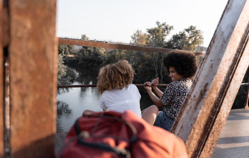 Back view of happy african american mom laughing near smiling daughter sitting on weathered bridge at sunset