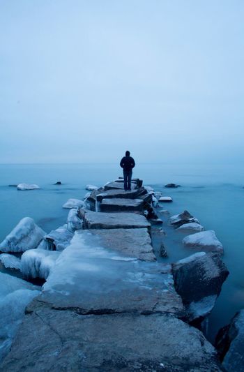 Rear view of person standing on stone pier during winter