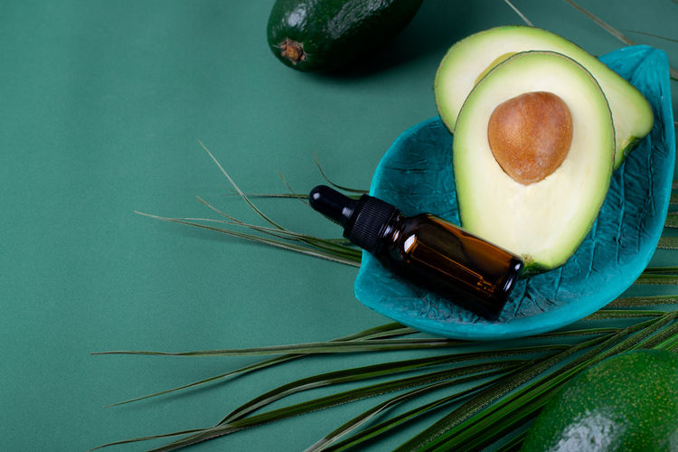 Avocado oil in dropper bottle and avocados on the green background. natural cosmetics 