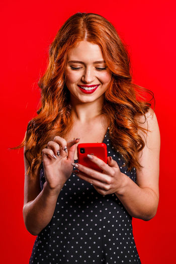Portrait of smiling young woman using phone against red background